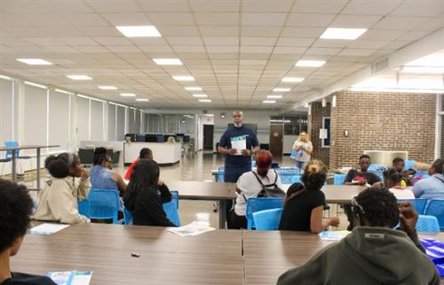 man standing in room in front of people talking